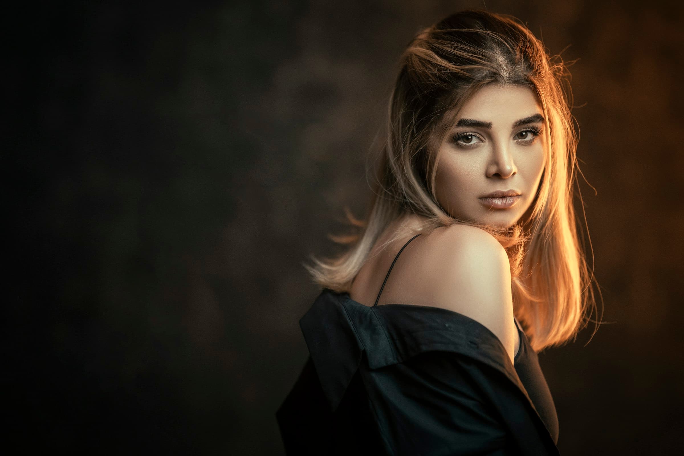 Portrait of a woman with glossy, honey-toned hair in warm studio light